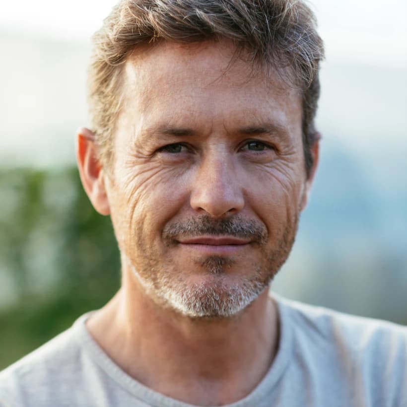 A man with grey hair in a white t-shirt, smiling