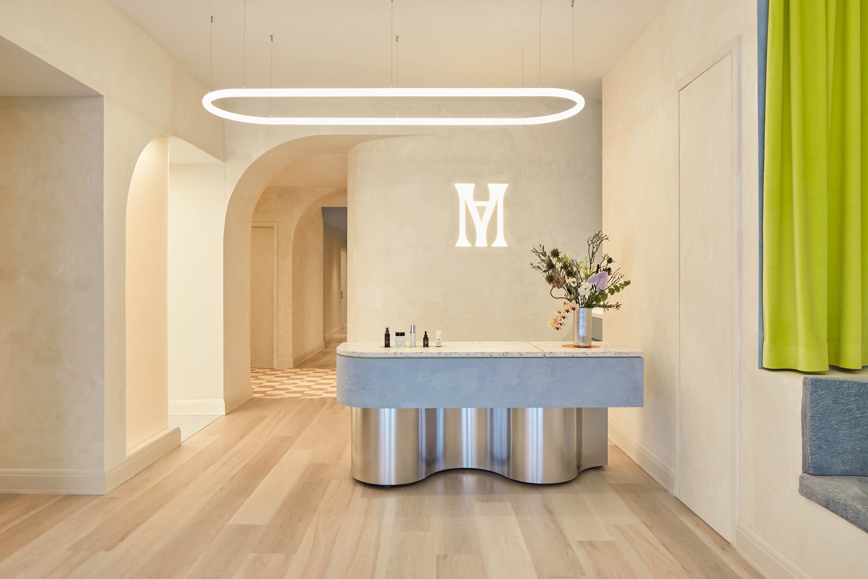 Reception at the Upper East Side studio: a curved desk under a ring light, the monogram on the wall behind it